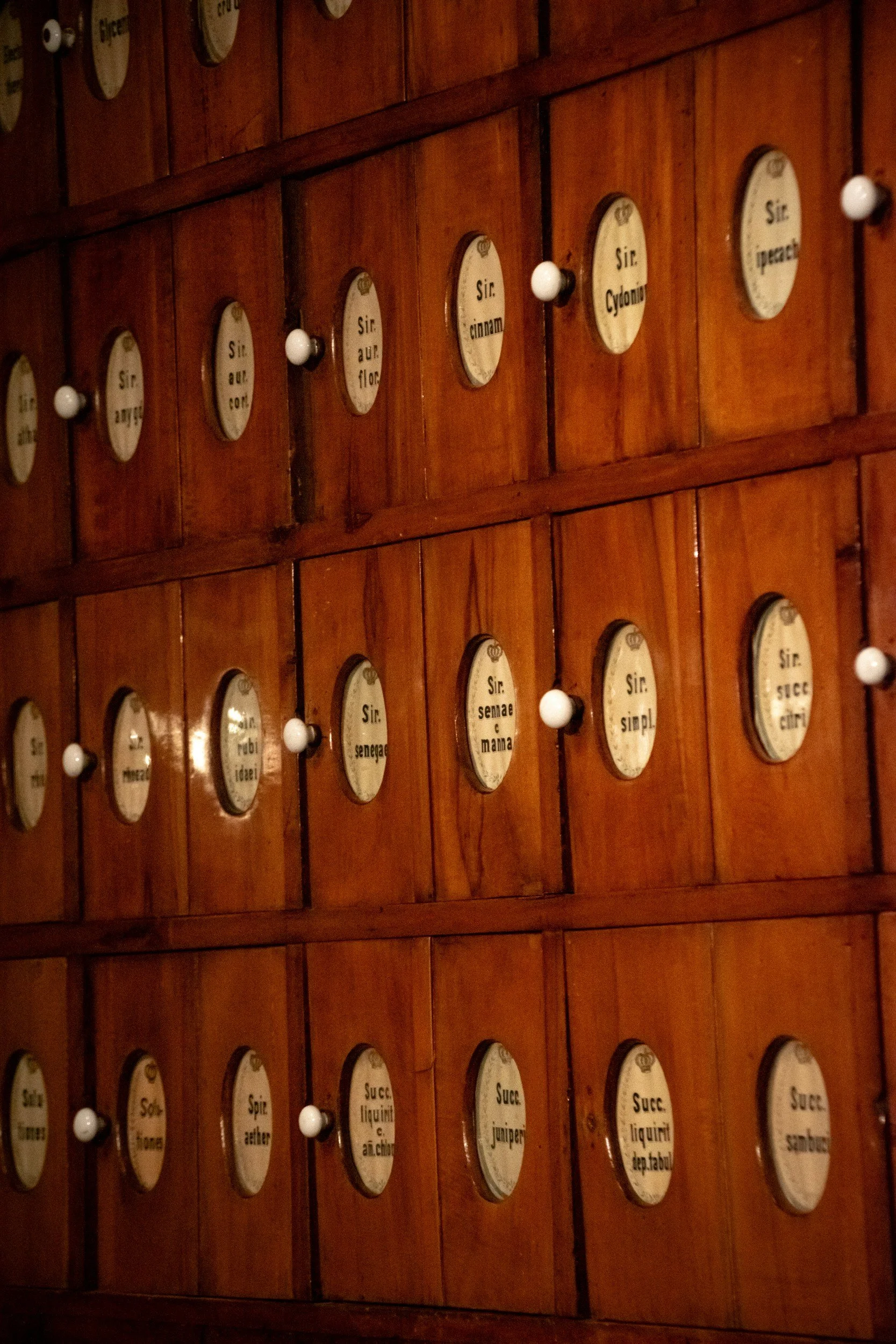 A wooden cabinet with multiple small drawers, each labeled with French spice names such as Sir. cinnamon, Sir. auber con, Sir. cyanm, Sir. demer, and others.