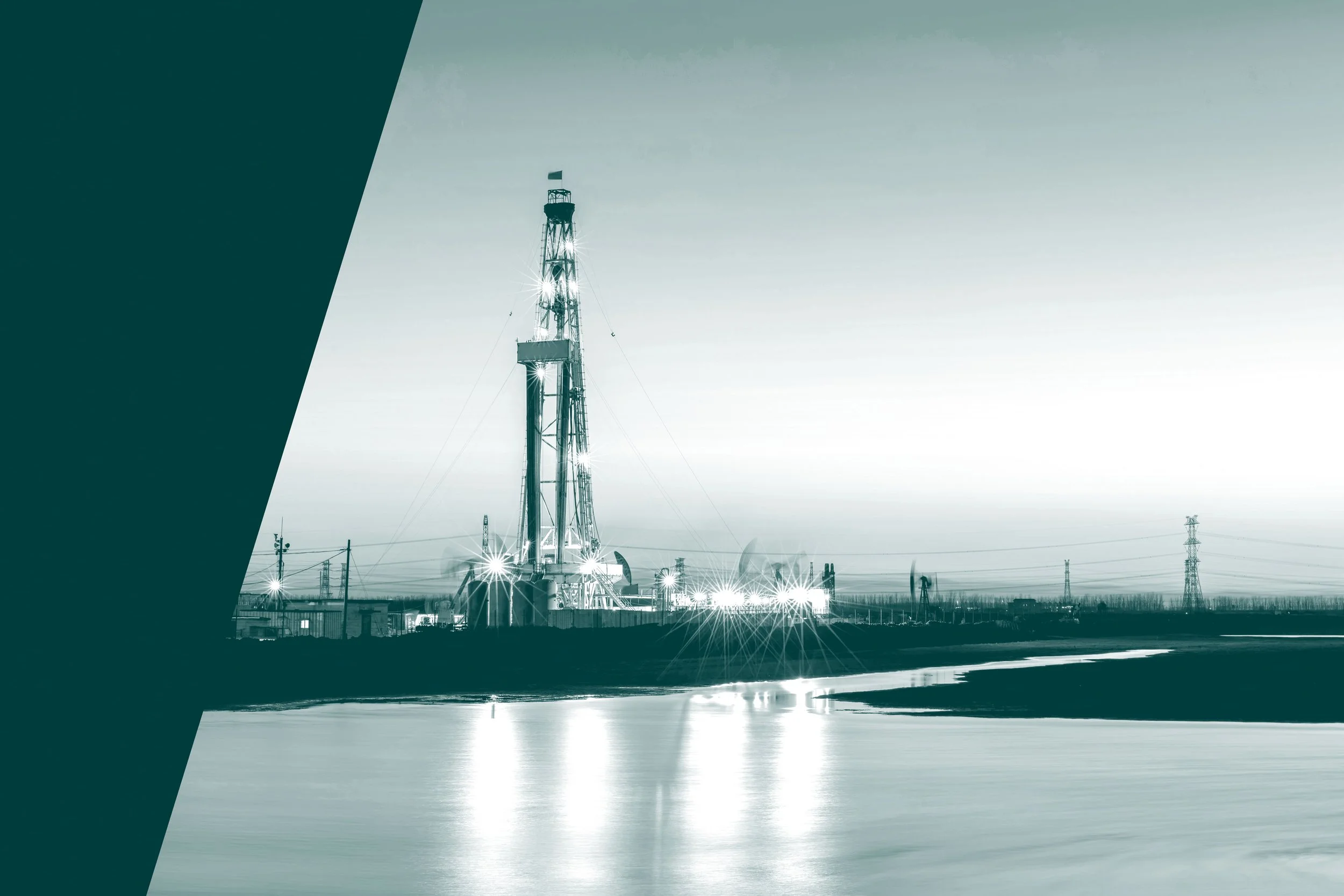An oil and gas operation site, surrounded by power lines and infrastructure, reflected on a calm body of water, with an overcast sky in the background.