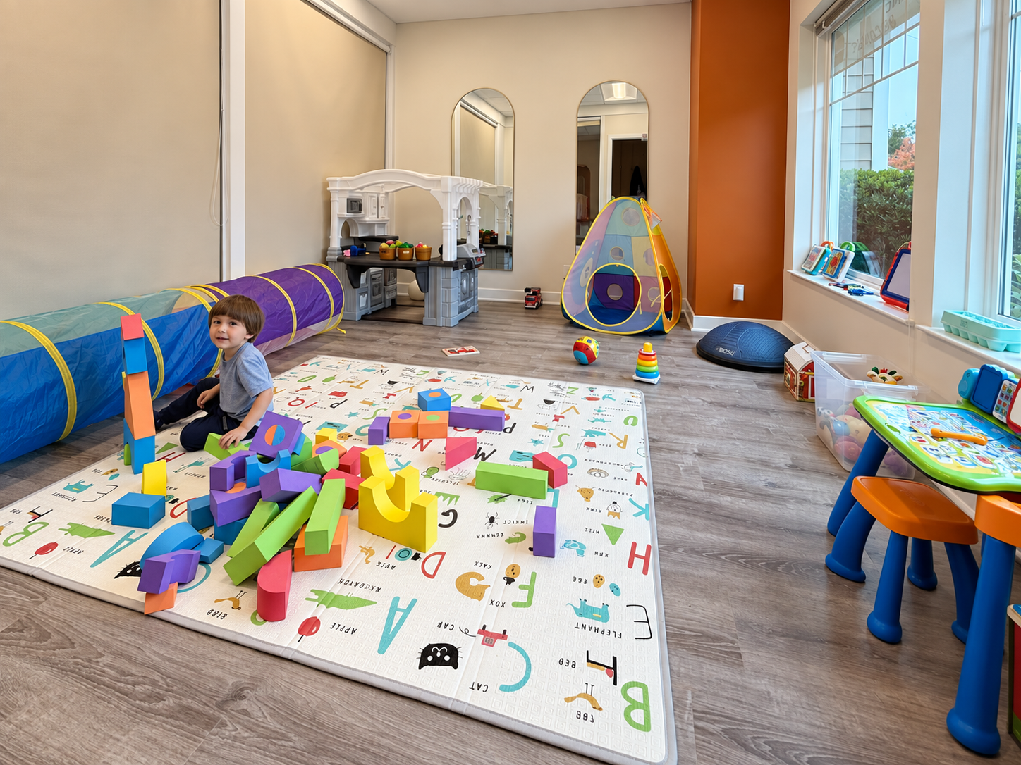 Kids Club playroom at Discipline Wellness with colorful toys, a play mat and a child playing.