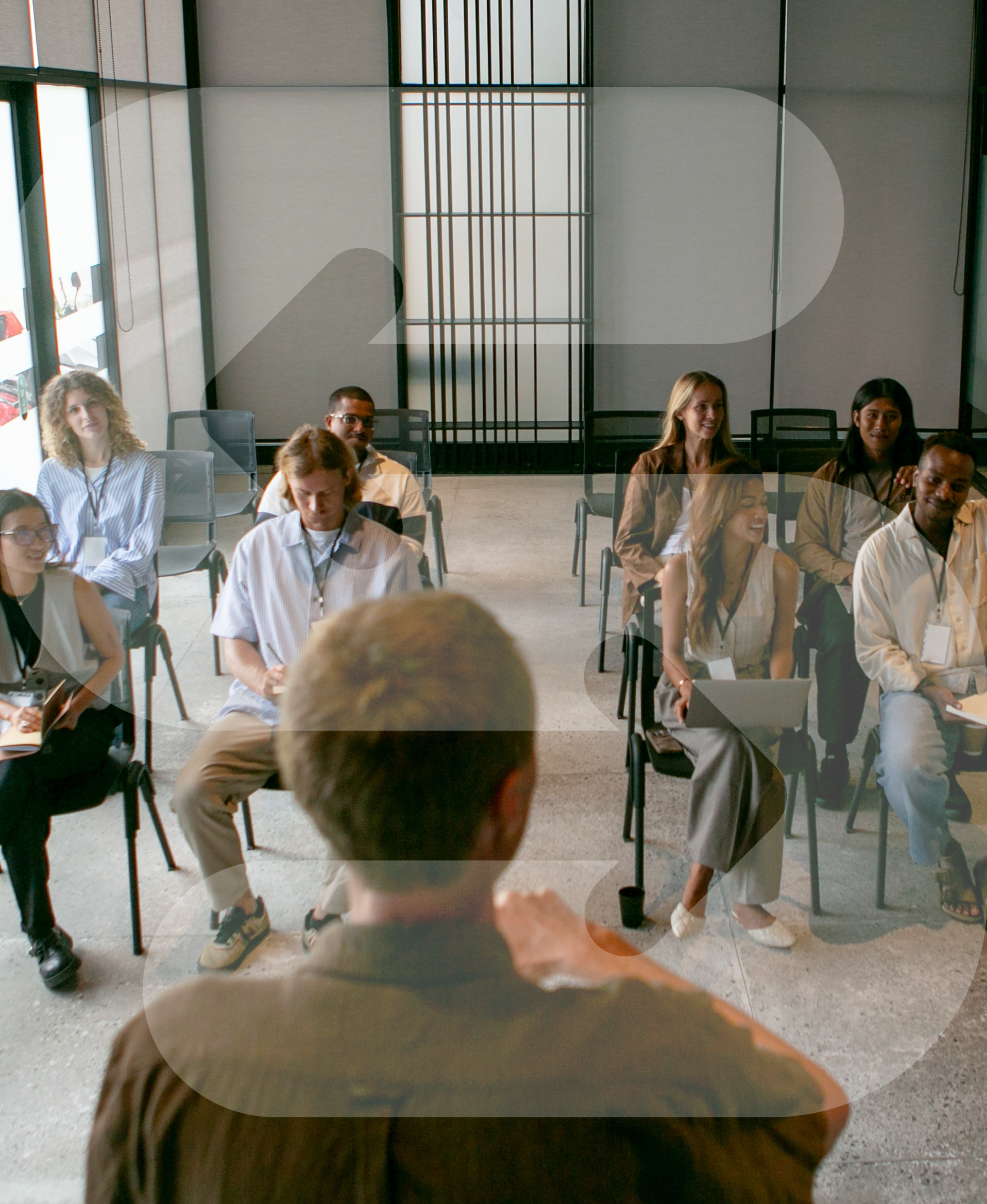 People seated in a modern conference room with large windows and a decorative wall.