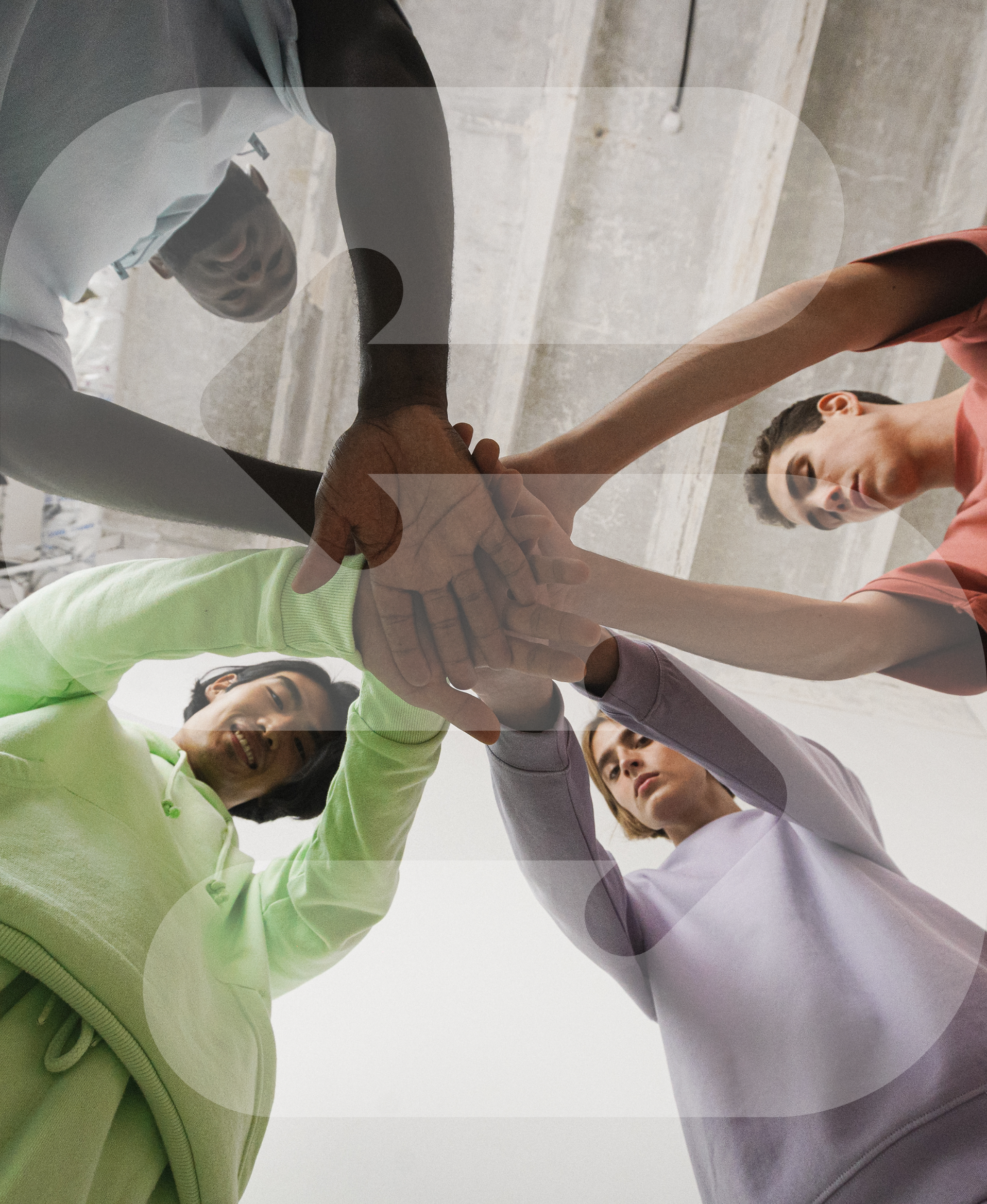 Group of diverse individuals in casual attire joining hands in a huddle, symbolizing teamwork or unity, with their faces visible and looking focused.