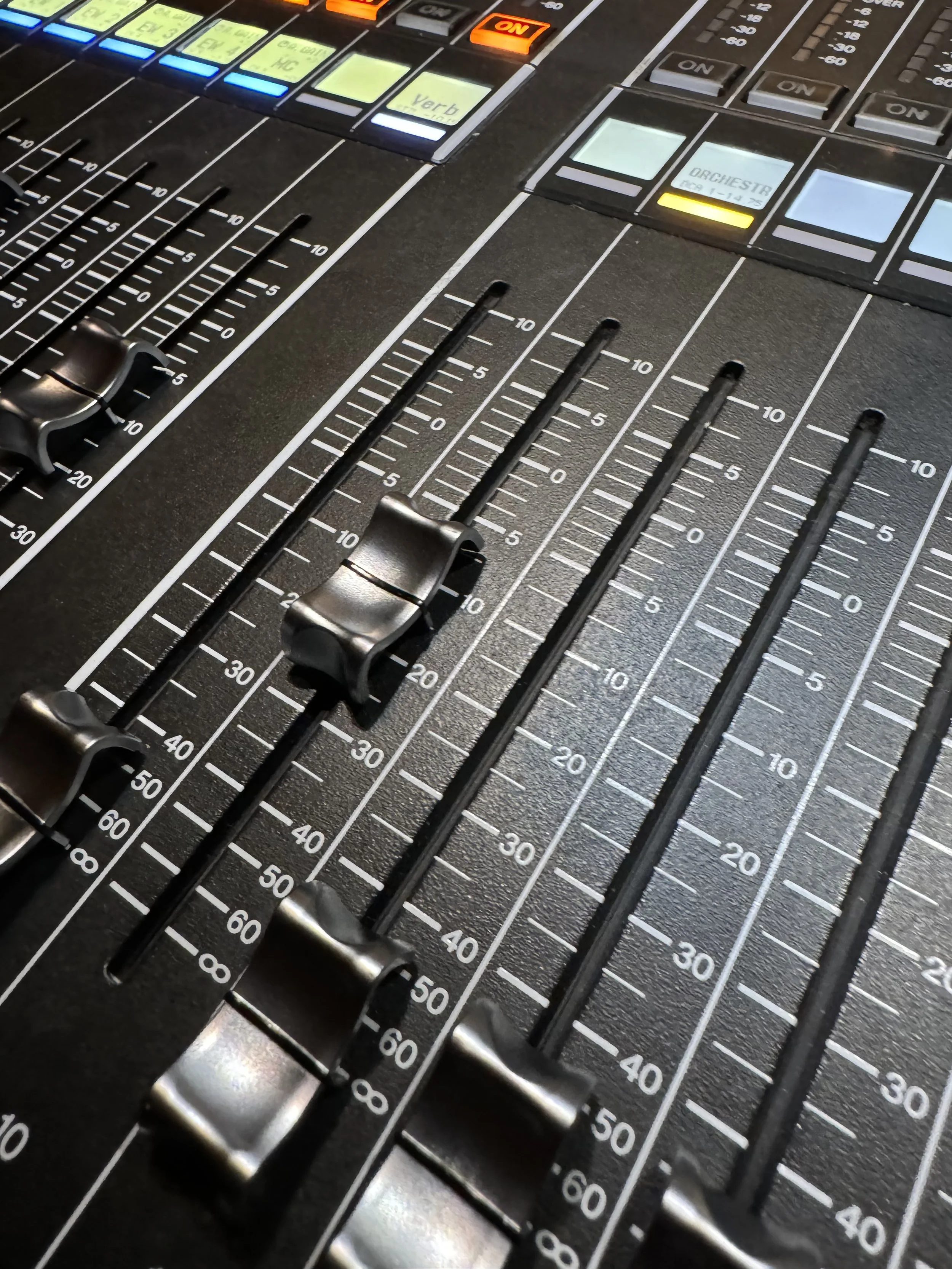 Close-up of a professional audio mixing console with sliders, buttons, and illuminated control panels.