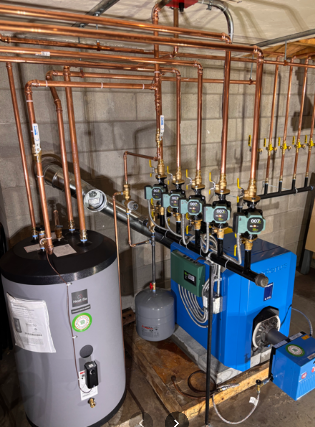 Industrial mechanical system with copper pipes, gauges, a water heater, and a blue heat pump system.