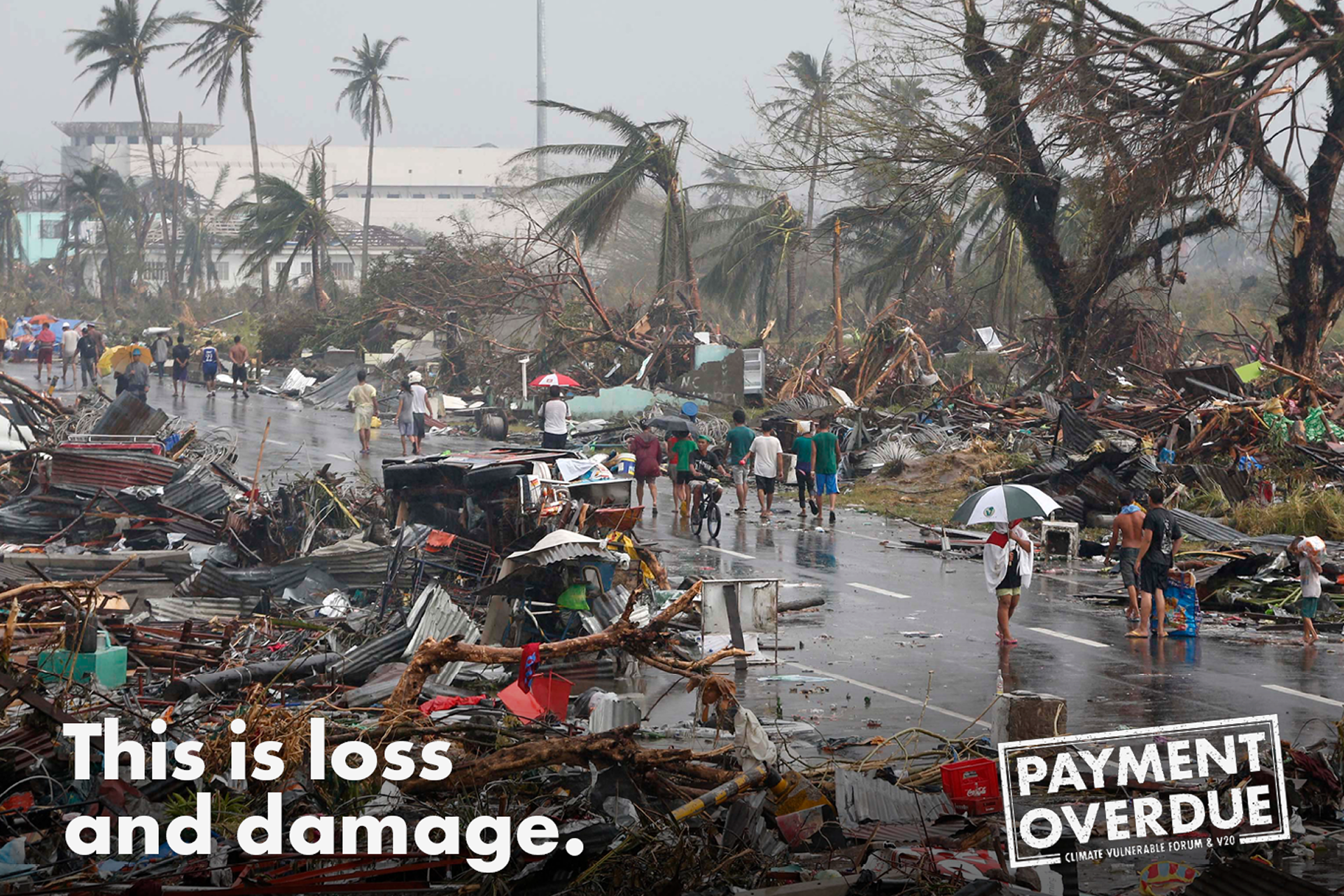 There is a road which has had a hurricane or floor move through it. All of the builds on it are wrecked, and people are walking down the street carrying their belongings. Over the top there is text that reads 'This is loss and damage'