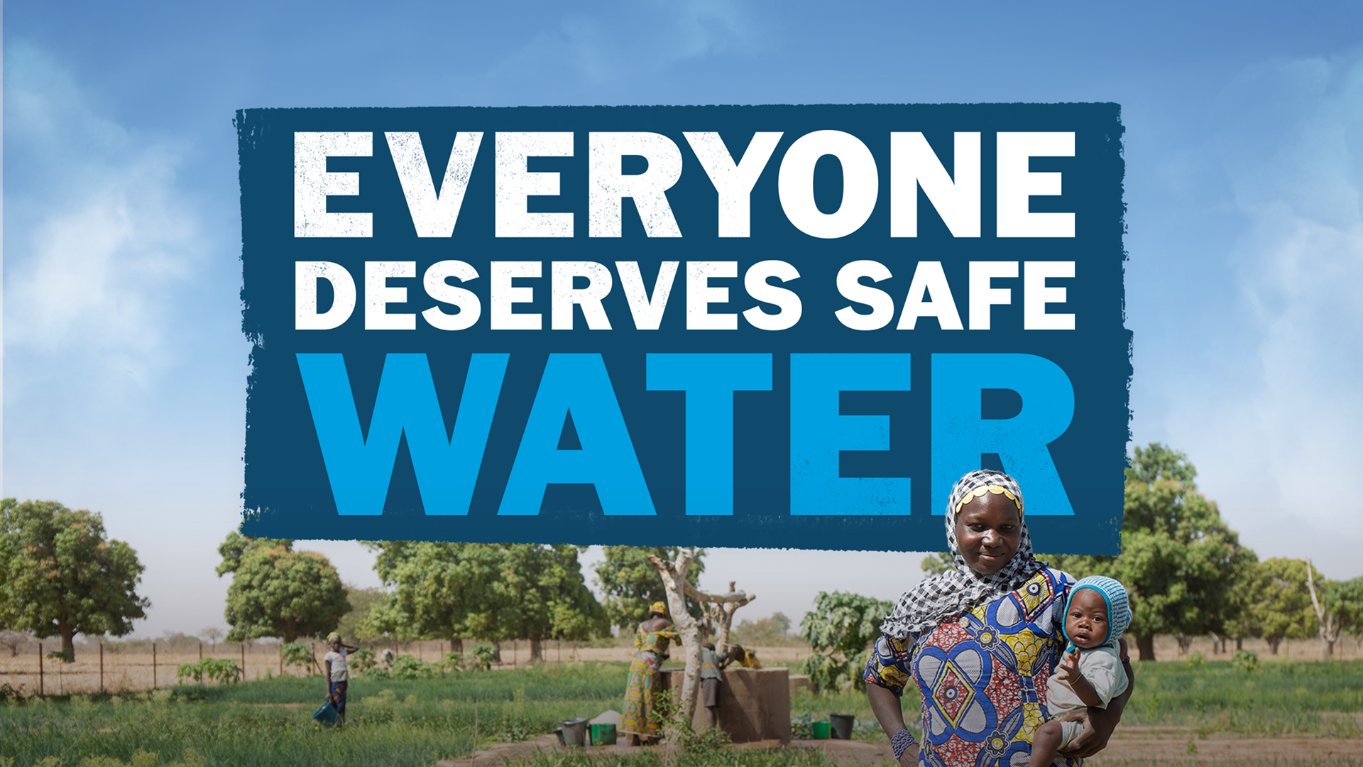 A person is stood in a field, holding a baby. Behind them is a pump, gathering water. There is a slogan behind them in the air which reads 'Everyone deserves safe water'