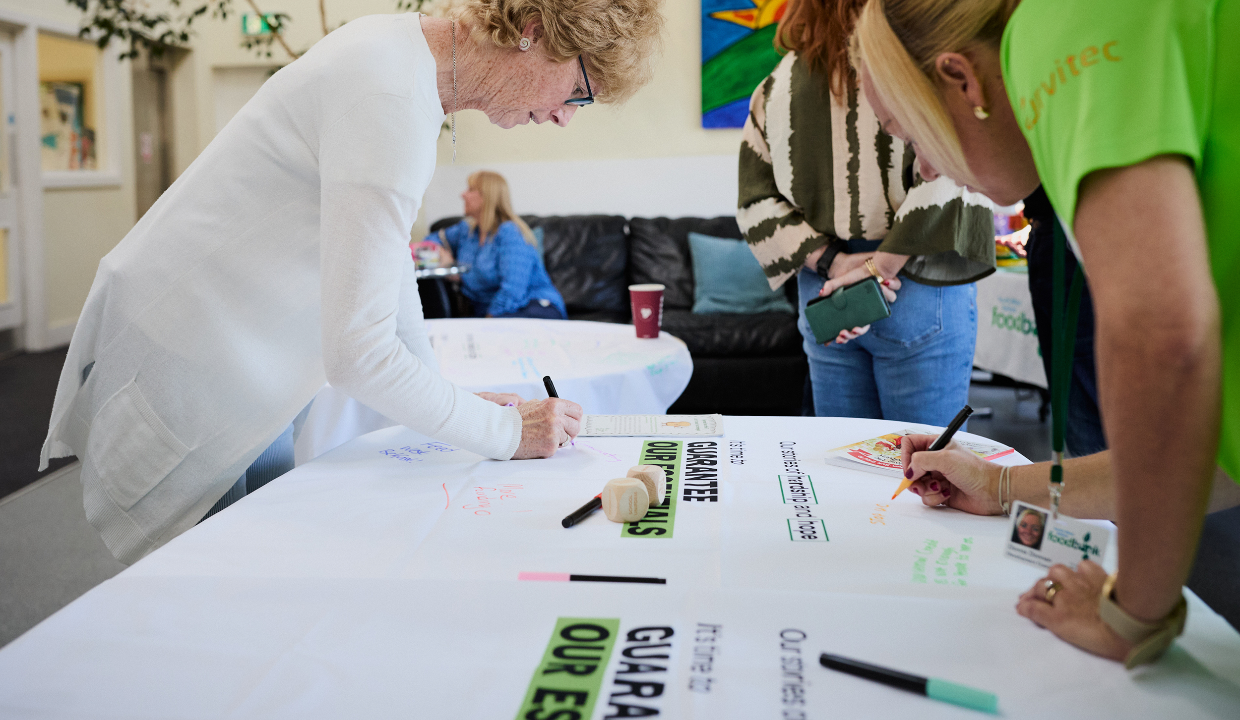 Three women are gathered around a table with a piece of paper on it. They are using coloured pens to write on the paper.