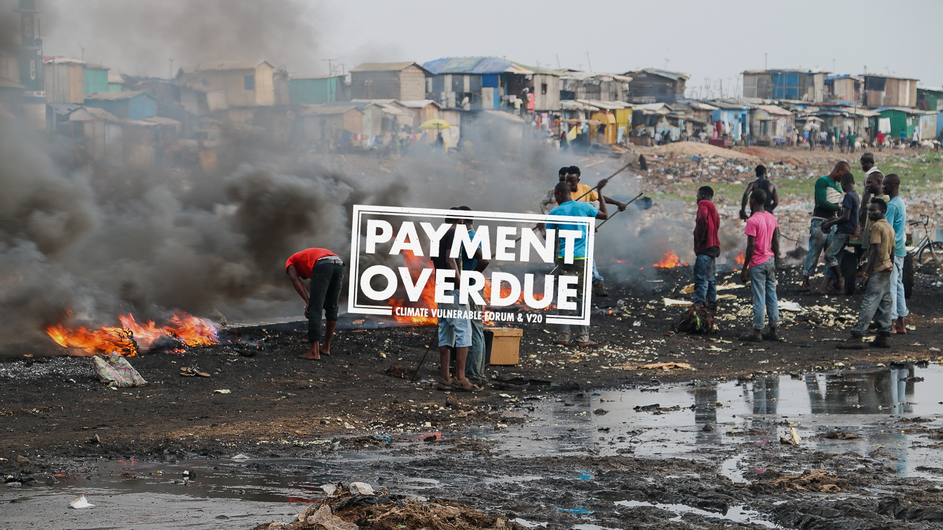 The image shows a burning pile of rubbish, with people stood around it. Over the top of it there is text that reads 'Payment overdue'