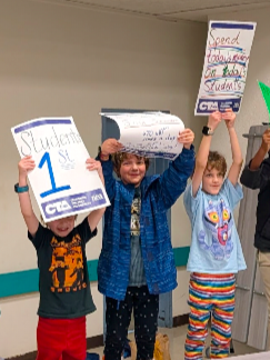 Children holding up handmade signs during a Oak Grove Board meeting, asking to support a pay increase for teachers and staff