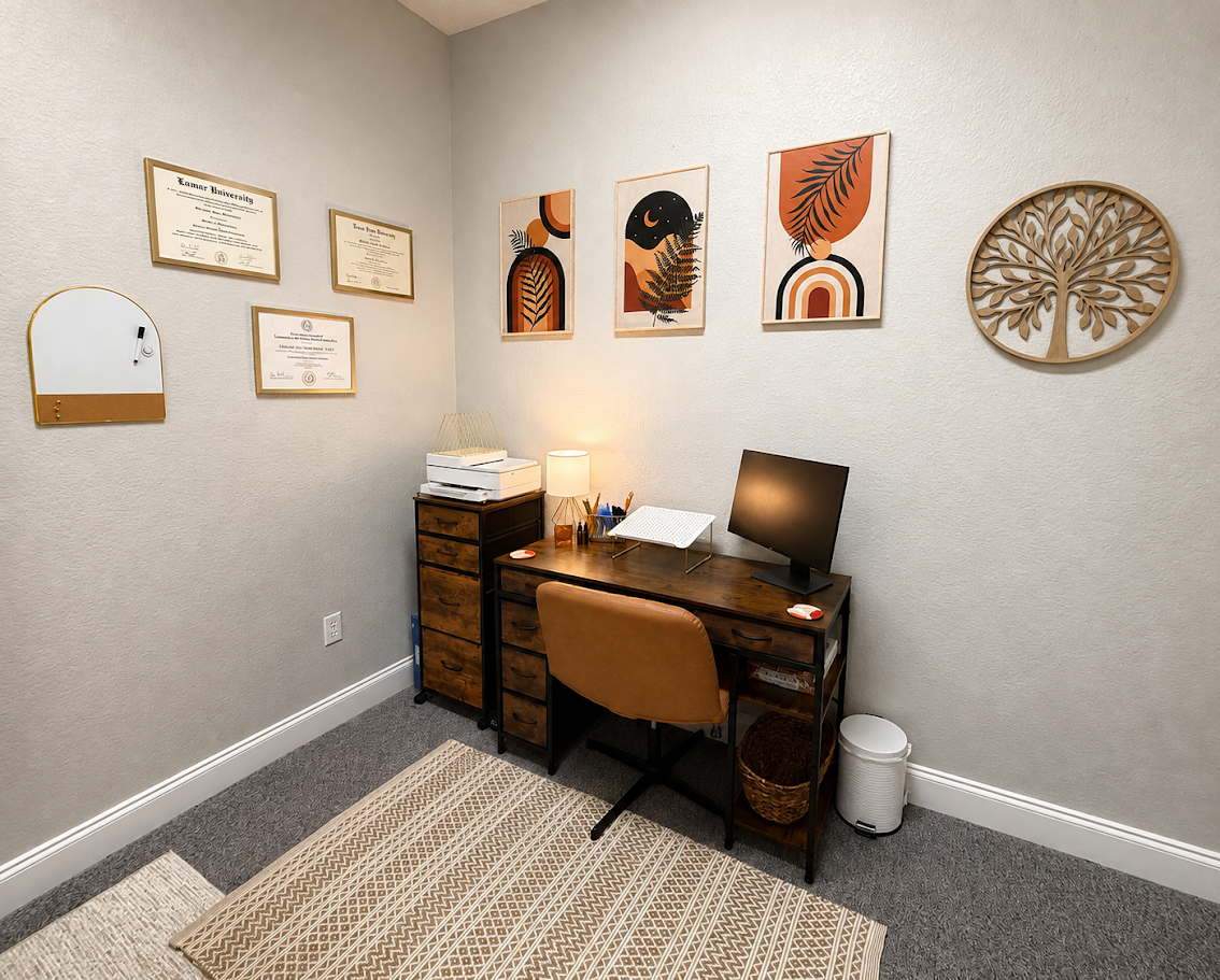 Small office with a wooden desk, leather chair, computer monitor, desk lamp, and art prints on the wall, including framed diplomas, decorative art, a wooden tree sculpture, and a knit rug on gray carpet.