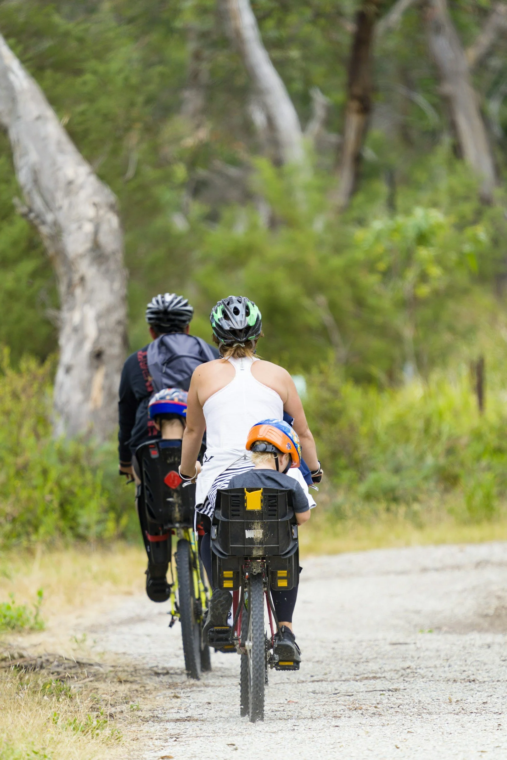 A group of people with helmets riding bicycles on a trail through a forested area.