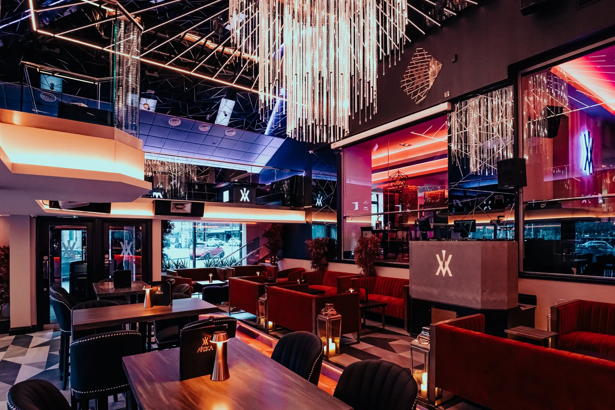 An upscale bar and lounge with modern decor, featuring a large chandelier with hanging crystal-like elements, neon lighting, and comfortable seating with plush chairs and tables.