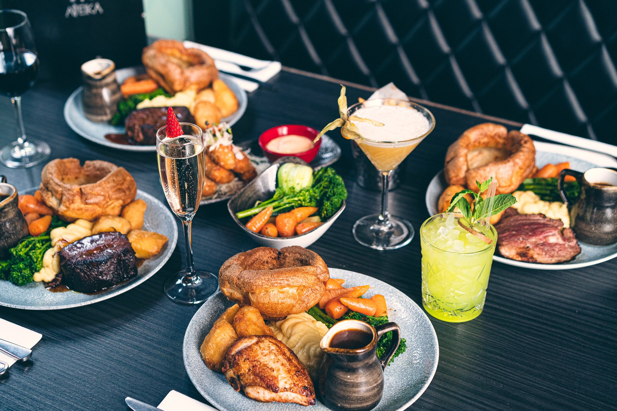 A table full of various breakfast foods including pastries, vegetables, meats, and drinks such as champagne, a cocktail, and a lime beverage.