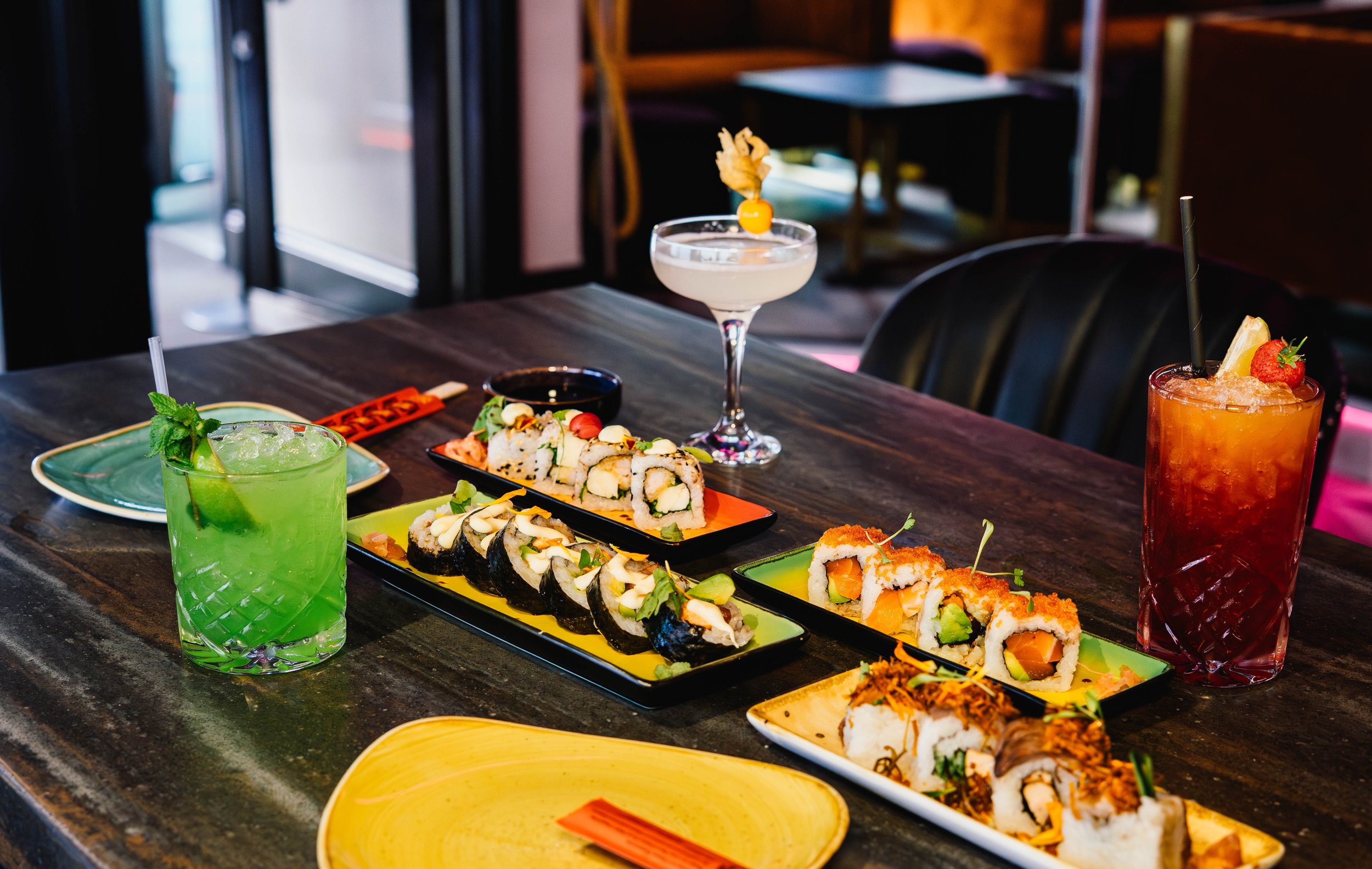 Assorted sushi rolls and drinks on a dark wooden table at a restaurant.