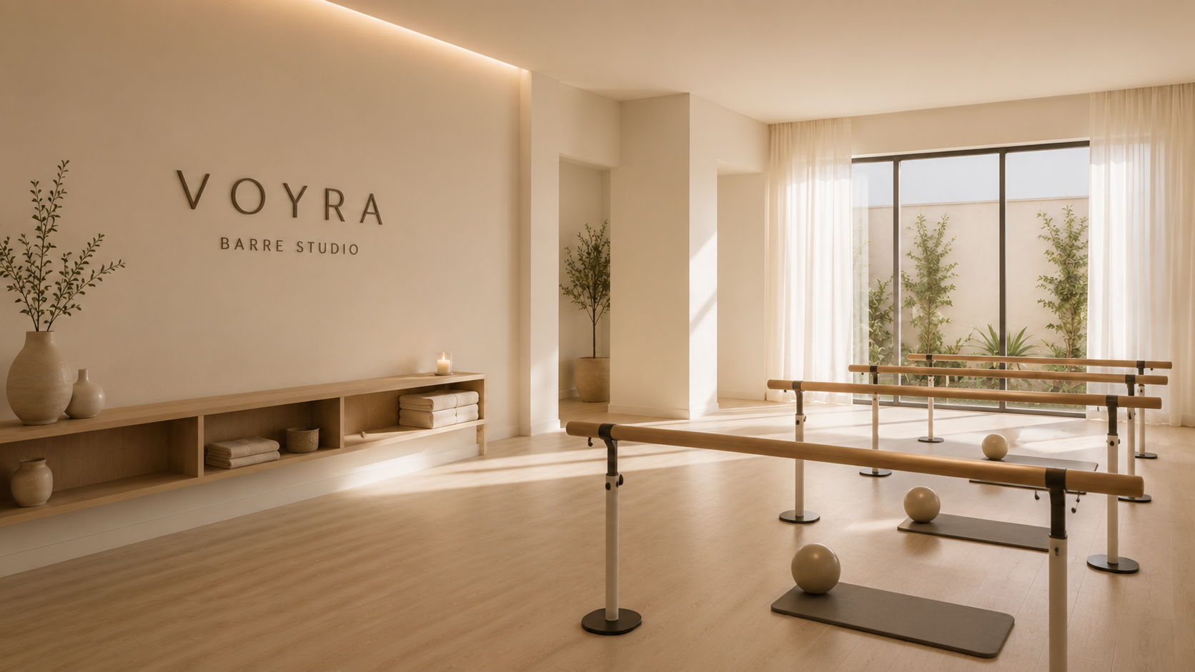 Estudio de ballet con barras de ballet, bolas y piso de madera, decorado en tonos claros con plantas y cortinas, y el letrero 'VOYRA BARRE STUDIO' en la pared.