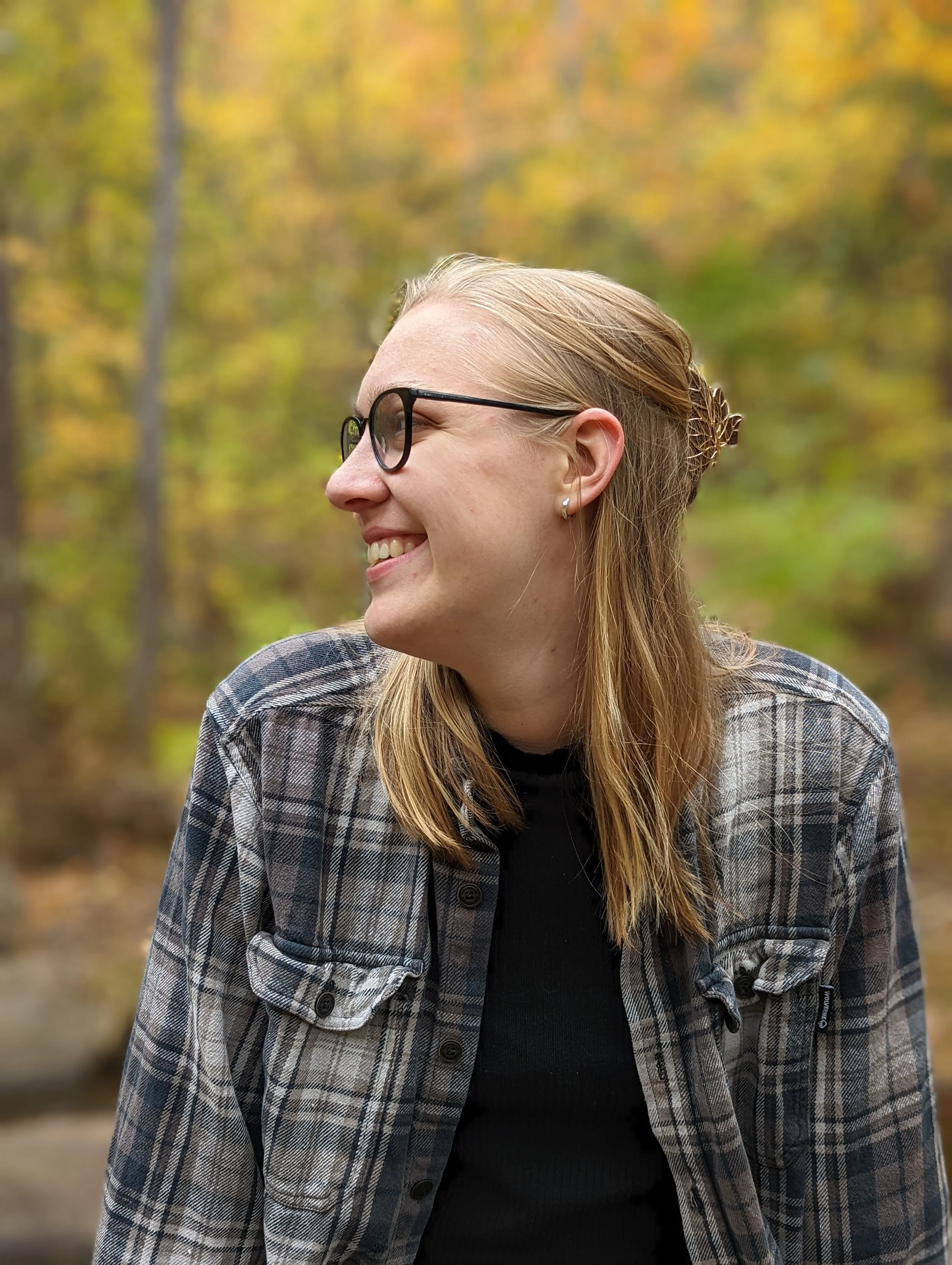jenna williams looking to the right. the trees have their fall foliage in the background.