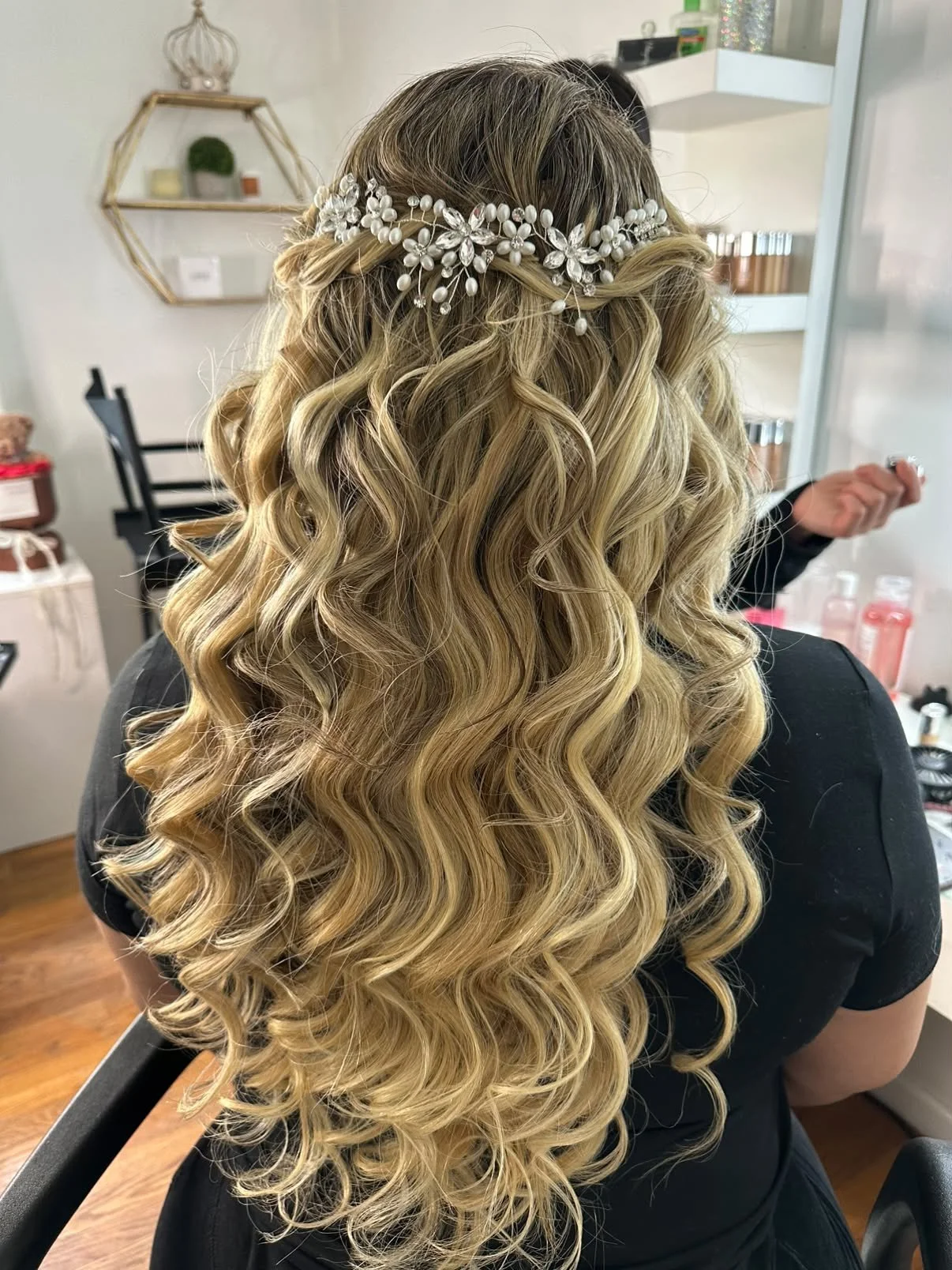 Back view of a woman with long, blonde, curly hair professionally styled by Brenda Rodriguez wearing a pearl and floral headband.
