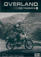 A person riding a motorcycle on a mountainous road at a high altitude, with the environment in the background. The image appears to be in black and white.