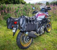 A motorcycle parked on grass with a scenic background of bushes and flowers.