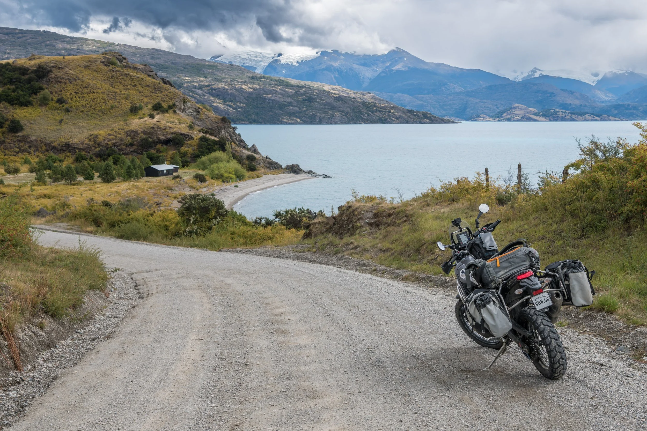 Motorcycle with saddlebags parked on a dirt road overlooking a lake and mountains in the distance.