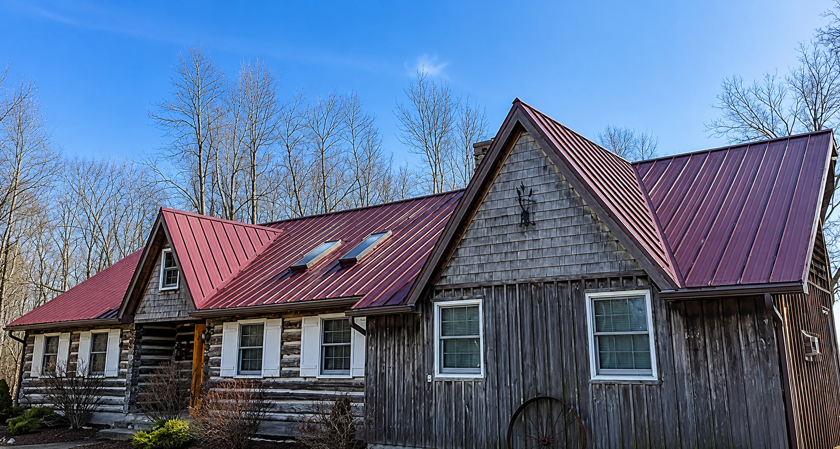 A rustic house with a red metal roof and wooden siding, surrounded by leafless trees against a clear blue sky.