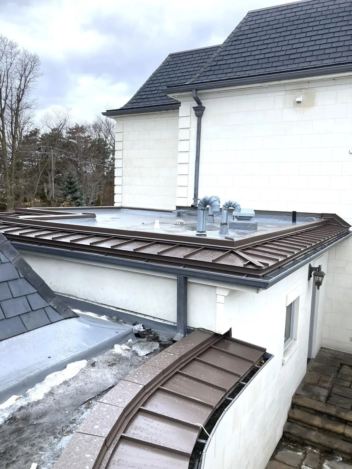 Roof with ongoing repairs, green pipes, and vent. Tree and cloudy sky in background.