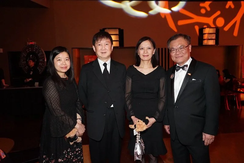 Four people dressed in formal black attire standing together indoors at a social event.