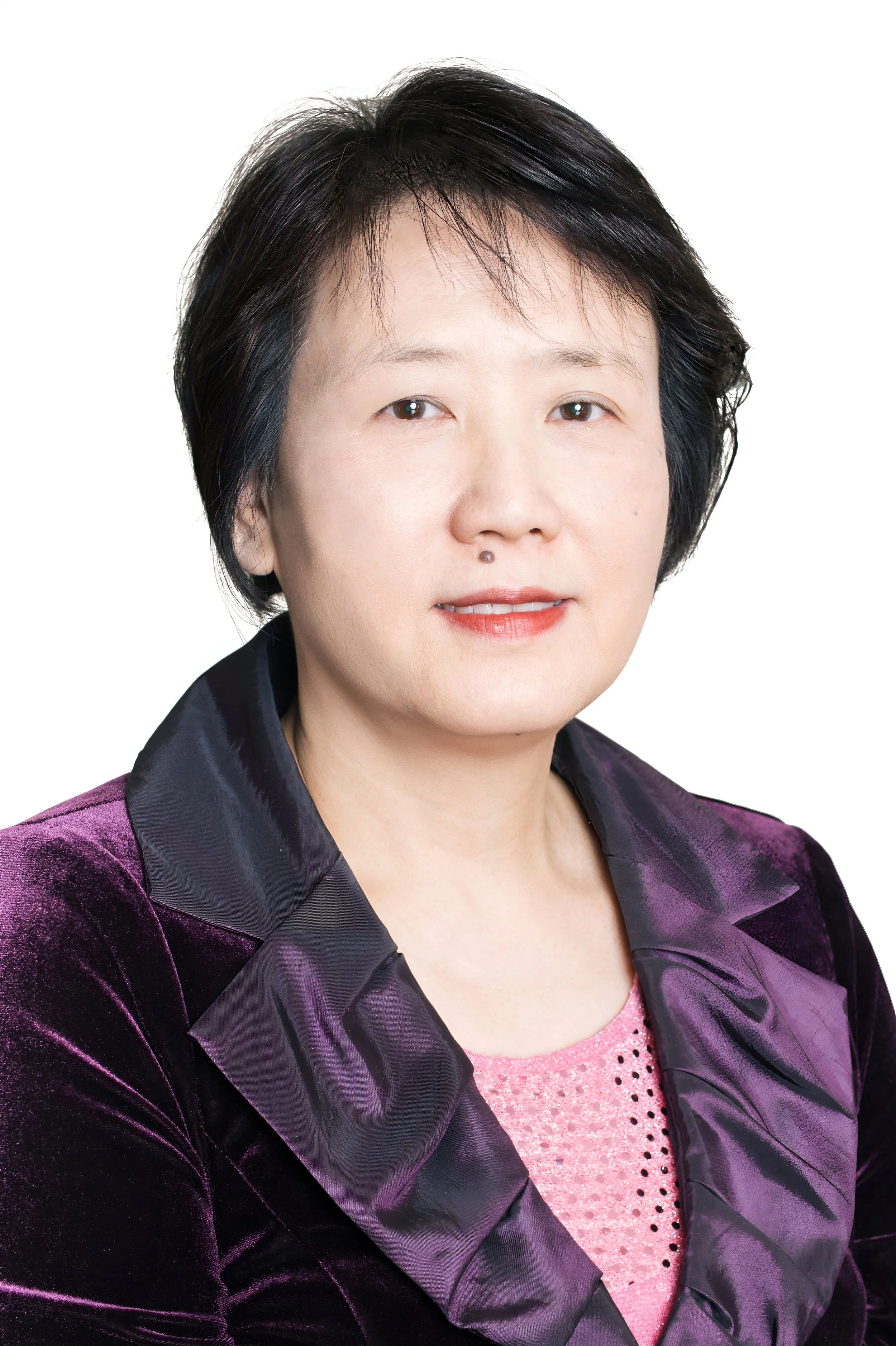 A woman with short black hair, wearing a purple velvet blazer over a pink top with a beaded neckline, smiling against a white background.