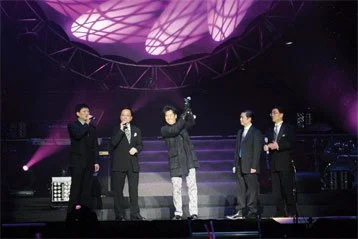 Five men standing on a stage with purple lighting, one holding a trophy, possibly during an award ceremony.