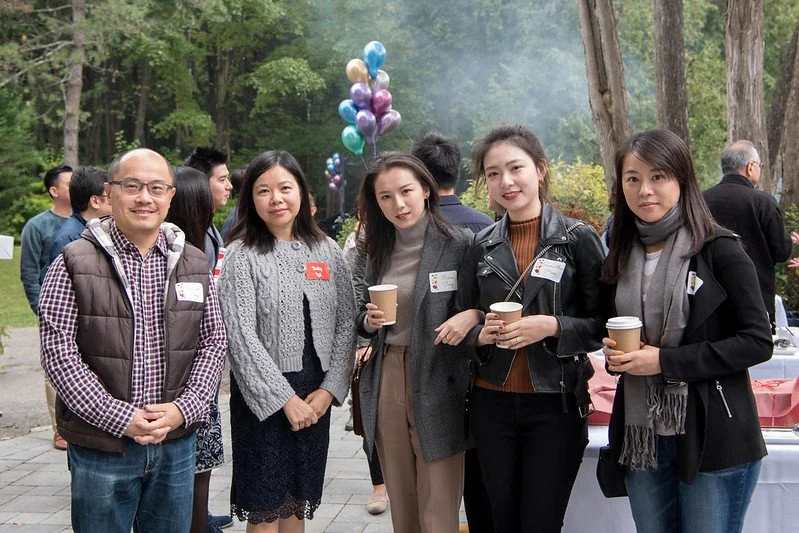 Group of five people standing outdoors at a park event, holding coffee cups, with balloons in the background.