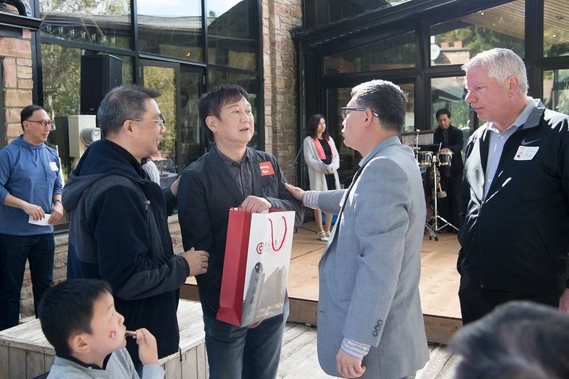 Group of people engaged in conversation at an outdoor event with a glass-walled building in the background.