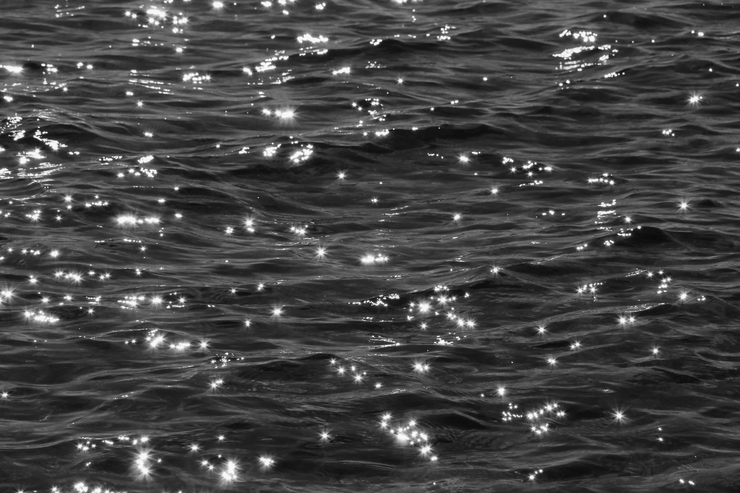 Black and white photograph of sunlight reflecting on the surface of the water, creating sparkling highlights.