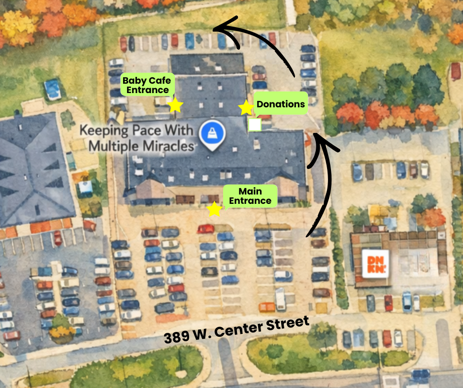 Aerial view of a building complex with parking lots. The main entrance is marked at the bottom, with a pathway leading to a second entrance labeled Baby Cafe Entrance. Near the second entrance, there is a donations area. The complex is surrounded by trees with fall foliage, and there is a street labeled 389 W. Center Street at the bottom of the image.