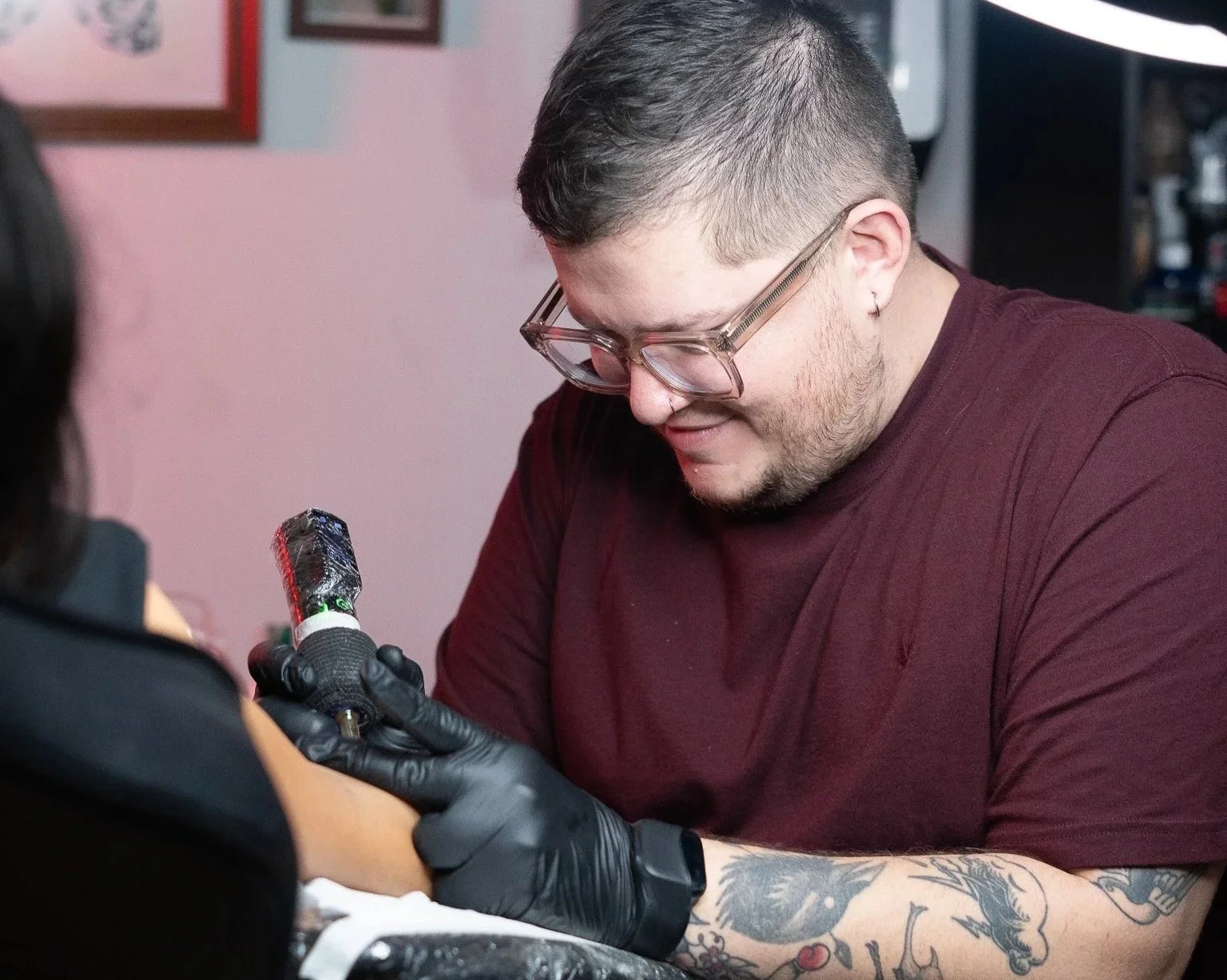 Hombre con gafas y tatuajes recibiendo un tatuaje en el brazo de un artista con guantes negros. Tatuador Benjamin Saenz, Antigua Guatemala, tatuando en Sublime Tattoo Antigua, tattoo shop