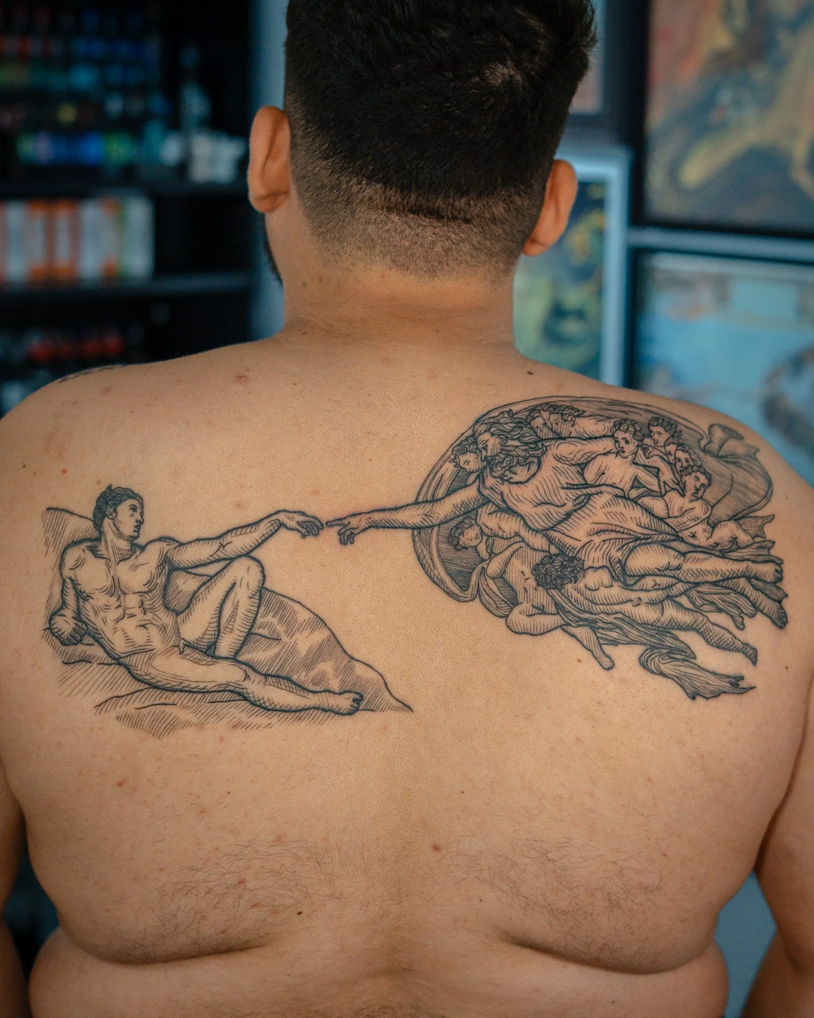La espalda de un hombre con tatuaje de La creación de Adán de Miguel Ángel y cabello corto, estilo grabado, etching, woodcut, linework, blackwork. Hecho en Antigua Guatemala, Guatemala. Tatuaje hecho por Benjamin Saenz en Antigua Guatemala. 