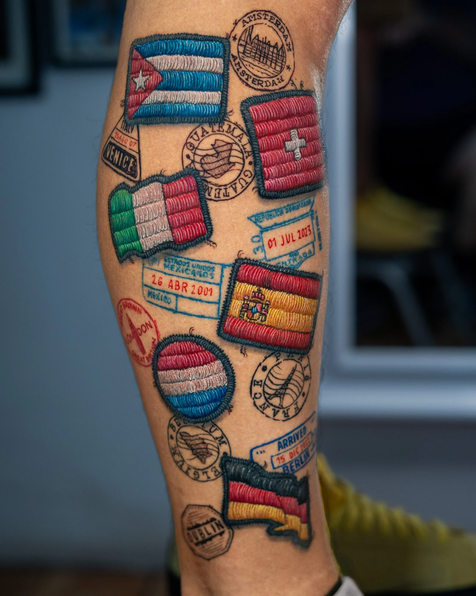 Tatuajes en pierna que representan banderas de diferentes países y sellos de pasaporte con fechas y nombres de ciudades.Tatuaje tejido, tatuaje con efecto de hilos. Tatuaje hecho por Benjamin Saenz en Antigua Guatemala, en el tattooshop: Sublime 