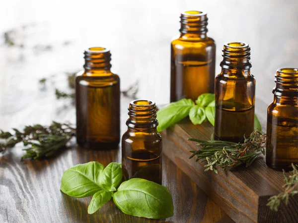 Several amber glass bottles and fresh herbs like basil and thyme on a wooden surface.