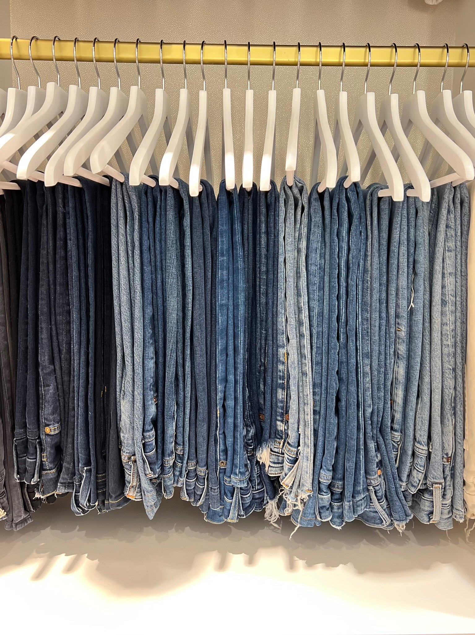 A clothing rack filled with various pairs of jeans in shades of blue and black, hanging on white plastic hangers.