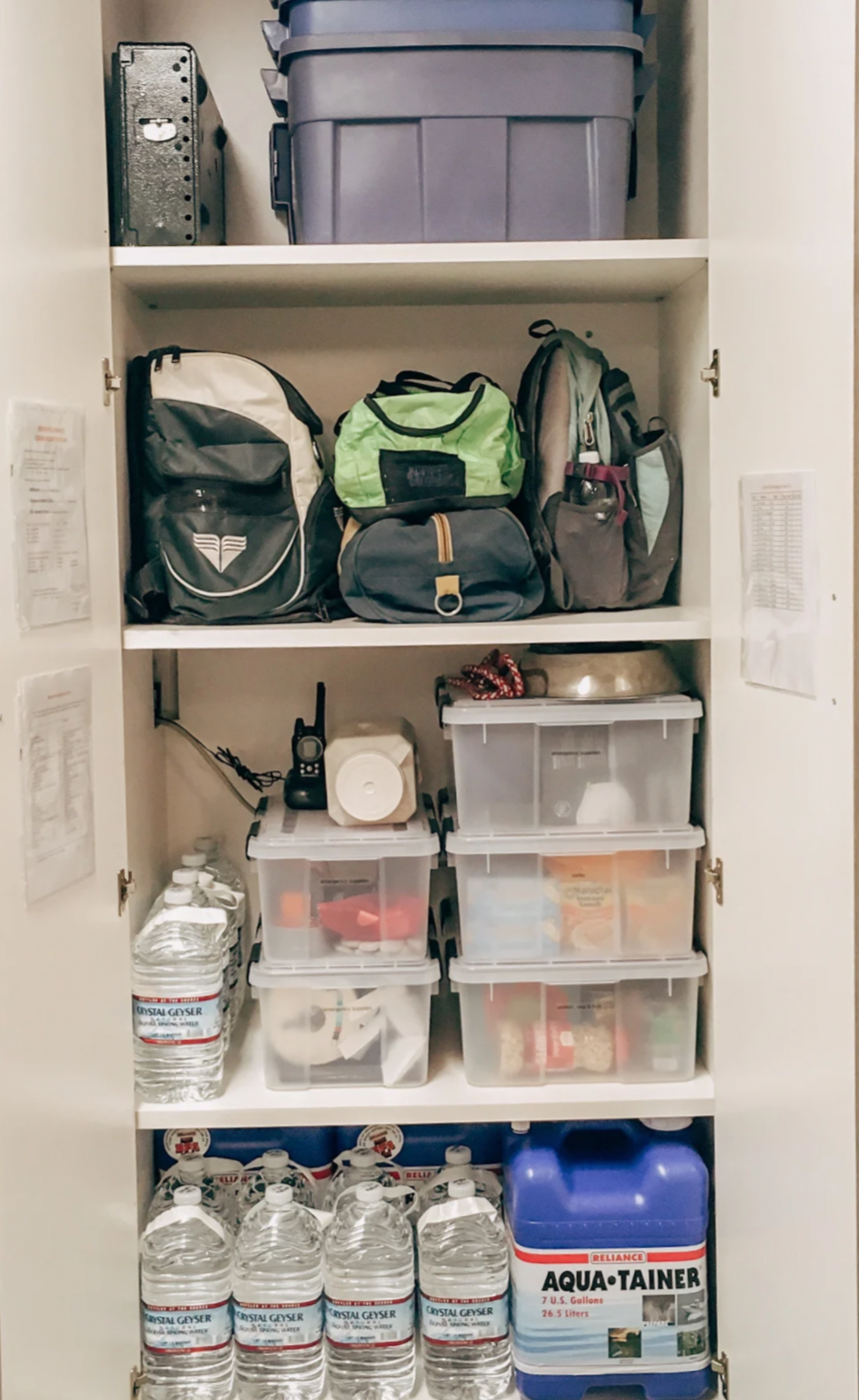 A pantry cabinet filled with water bottles, food, backpacks, storage bins, and miscellaneous items.
