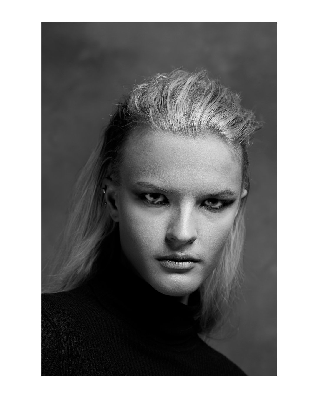 Portrait en noir et blanc d'une femme aux cheveux blonds et bouclés, portant un haut noir, avec un regard intense et expression sérieuse.