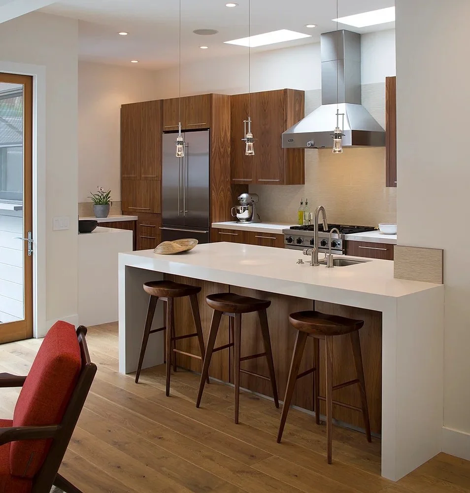 Modern kitchen with wooden cabinets, white countertops, three wooden bar stools at a white island, stainless steel appliances, and a paper pendant light fixture.