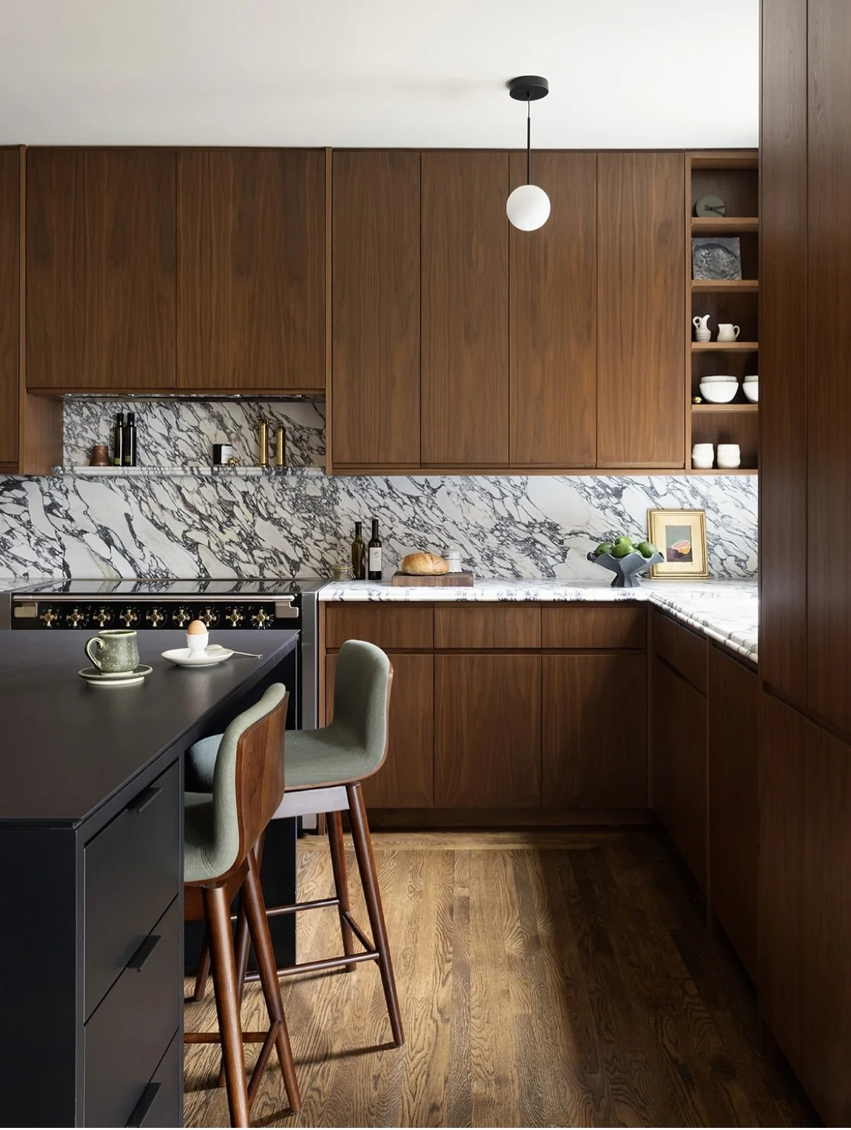 Kitchen with wooden cabinets, marble backsplash, black countertop, and green bar stools.