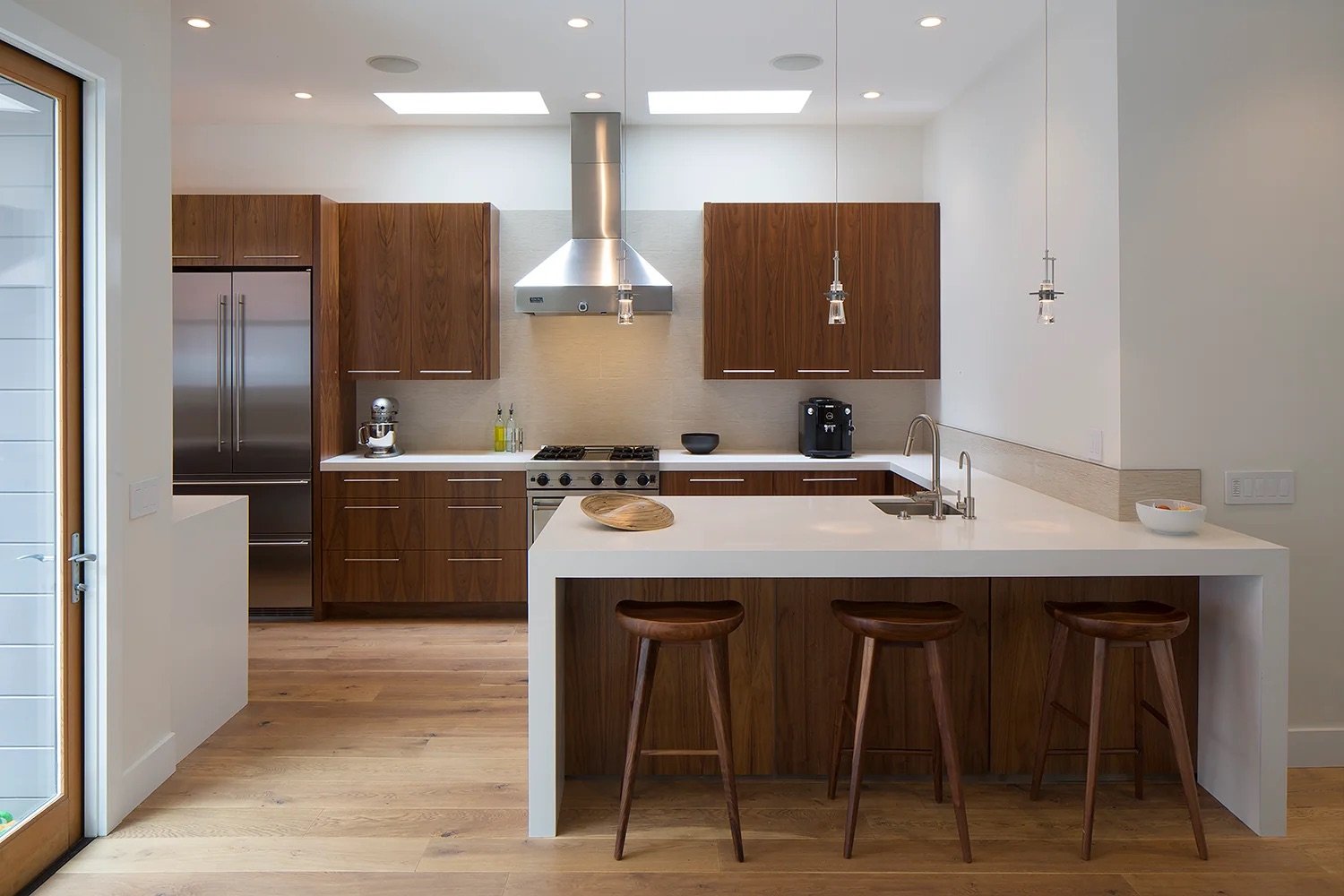Modern kitchen with wooden cabinets, stainless steel appliances, island with stools, pendant lights, and hardwood floors.