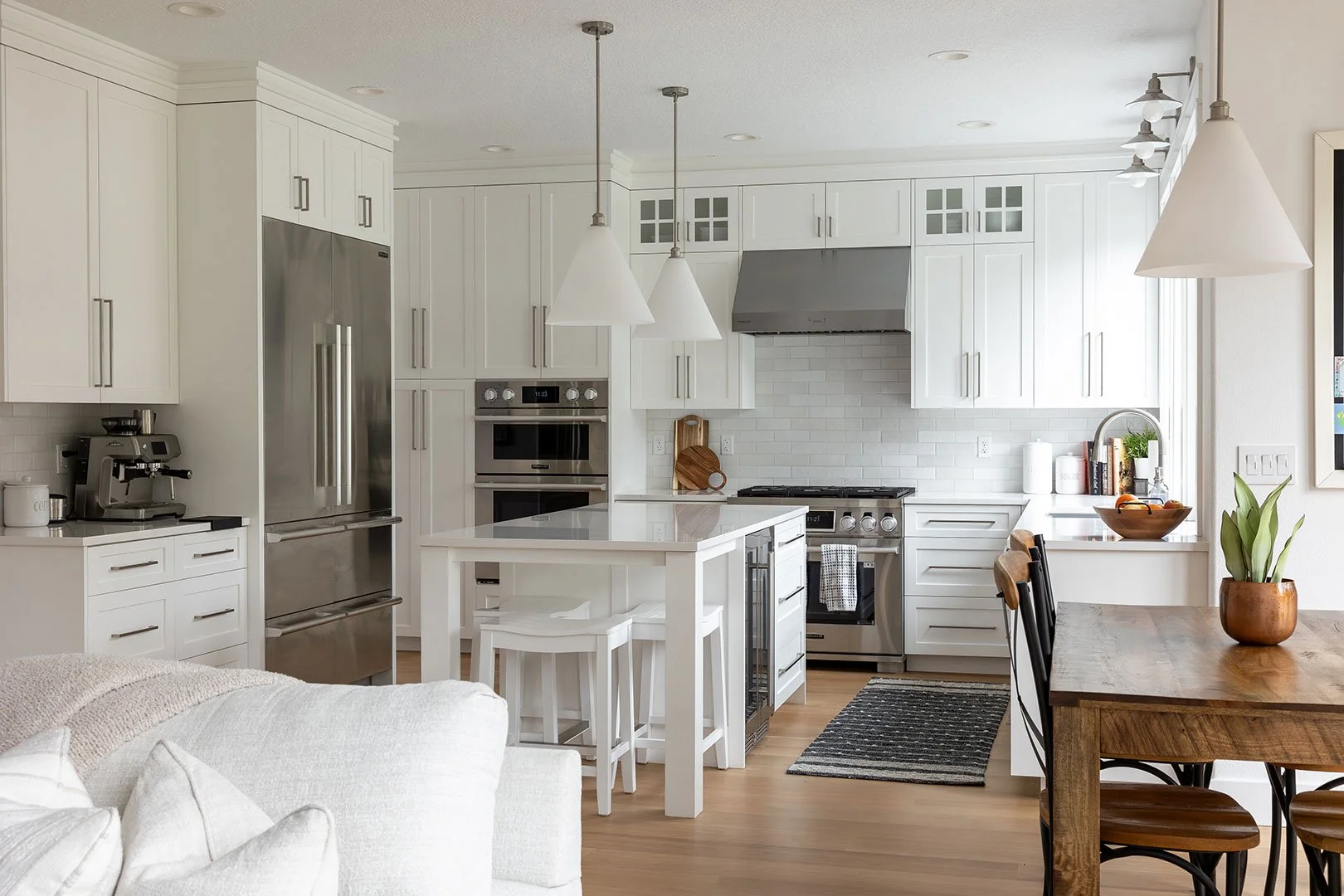 Bright modern kitchen with white cabinets, stainless steel appliances, and a wooden dining table with chairs.