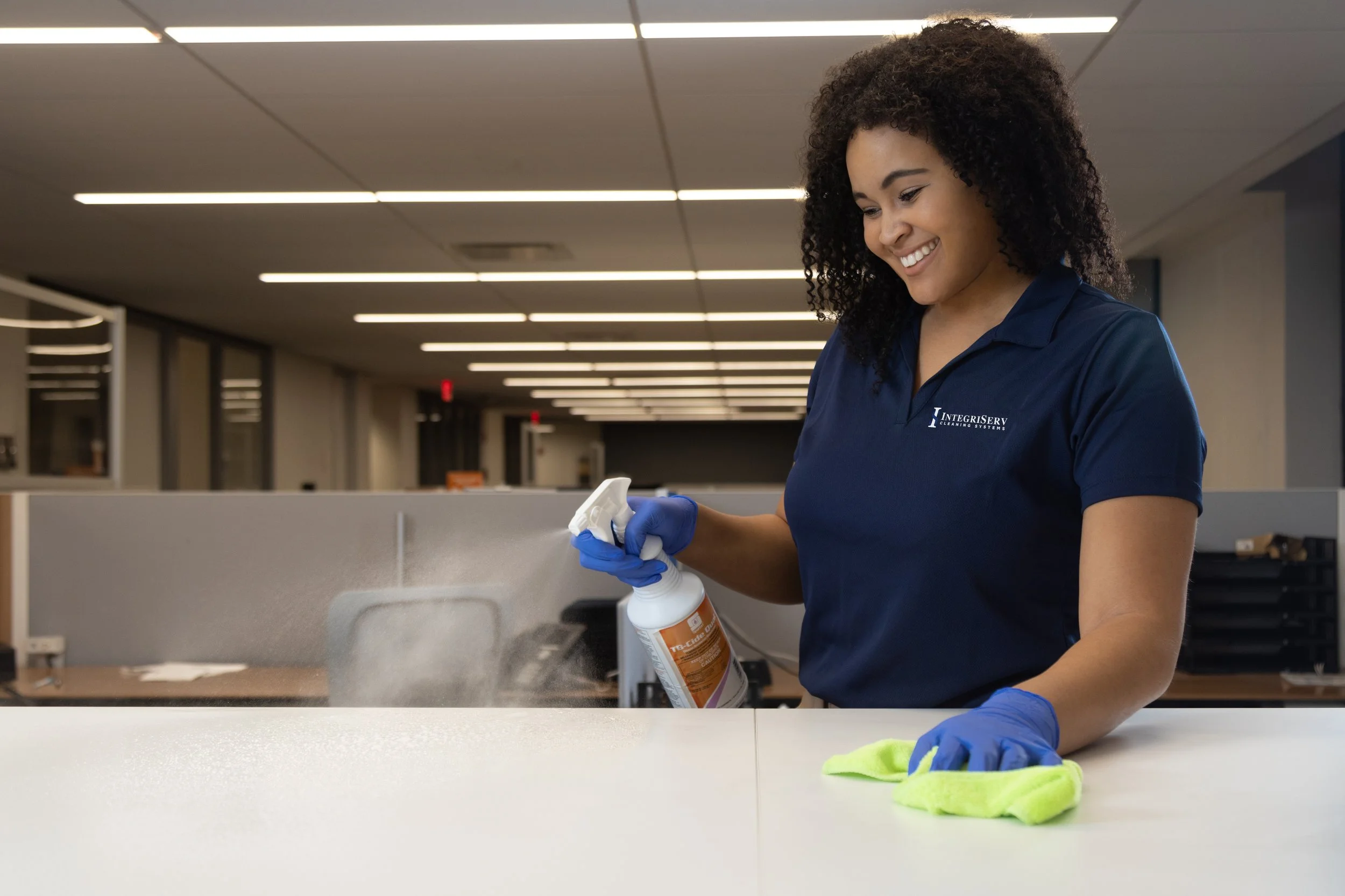 Professional cleaning technician disinfecting and wiping down an office desk with a microfiber cloth as part of routine commercial cleaning services.