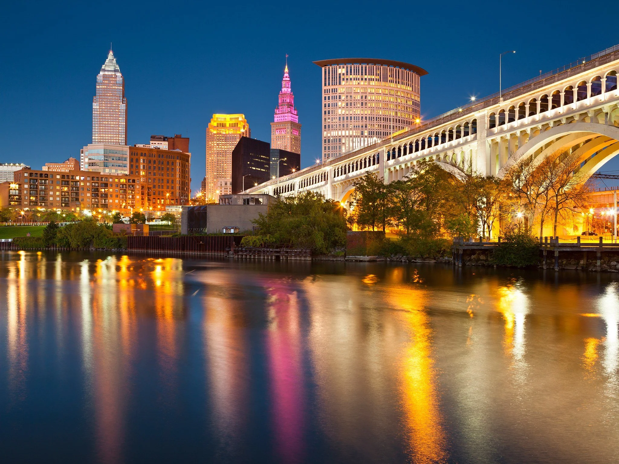 Cleveland, Ohio skyline at night with illuminated skyscrapers and the Detroit-Superior Bridge reflected in the Cuyahoga River.