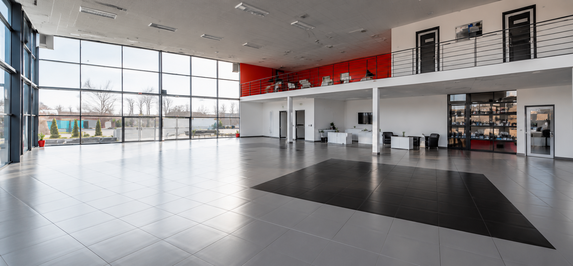 Spacious car dealership showroom with polished, spotless flooring and an open mezzanine level, showcasing the results of professional commercial cleaning services for automotive dealerships.