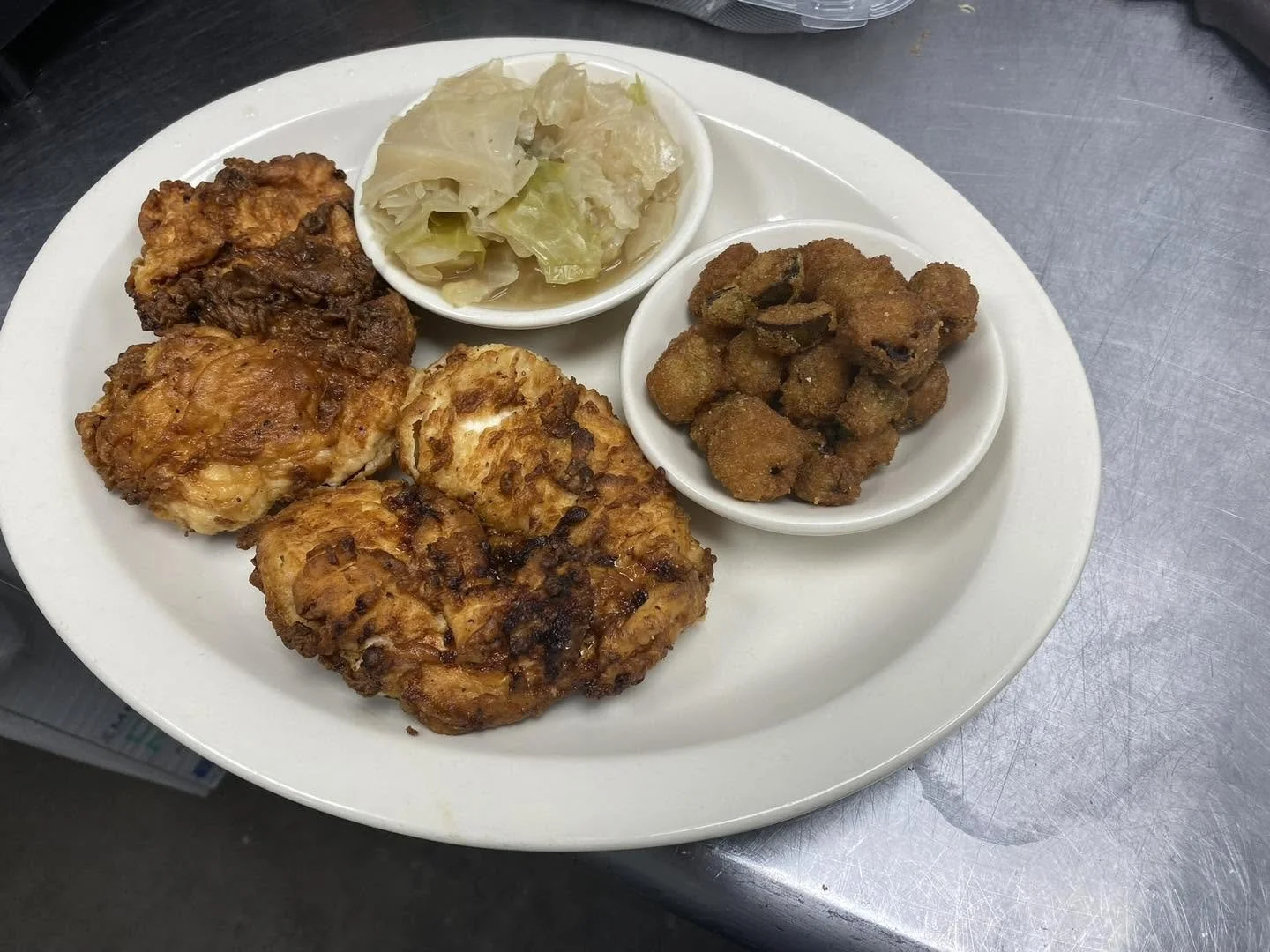 Plate with fried chicken, two types of cooked greens, and fried pork pieces.