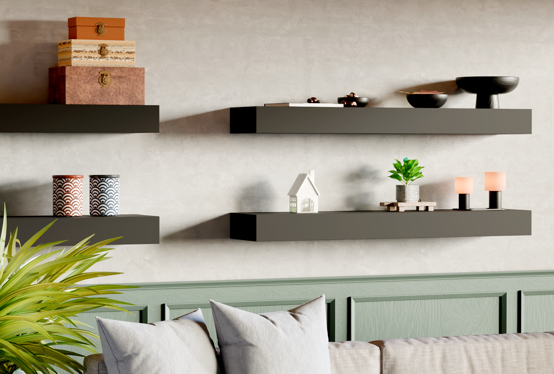 Living room corner with black floating shelves on light beige wall, decorated with stacked jewelry boxes, bowls, a small house model, potted plant, and candles, with pillows and a sofa below.