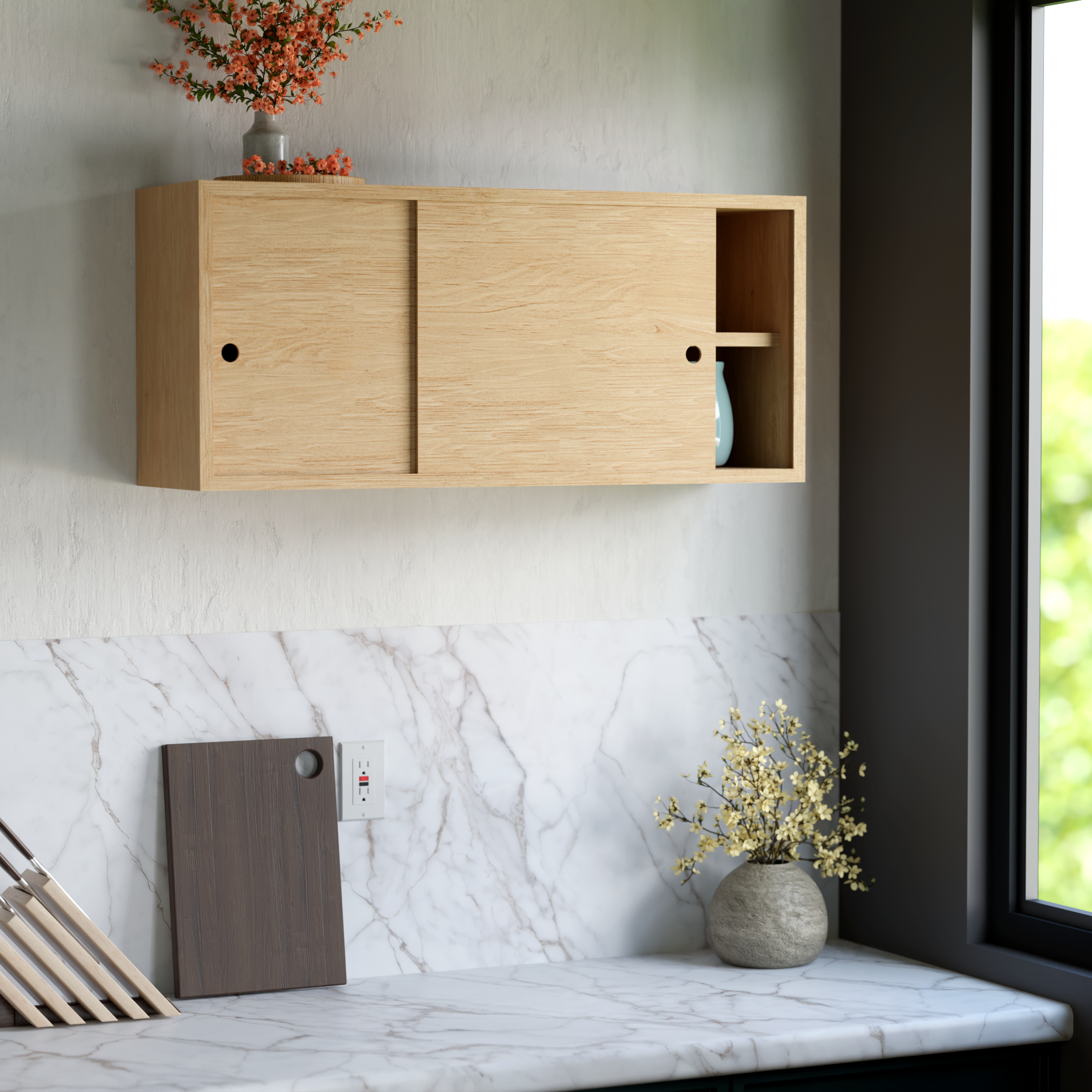 A modern kitchen countertop with a wood cutting board, a white vase with pink and orange flowers, and a gray vase in front of a marble backsplash near a window with greenery visible outside.