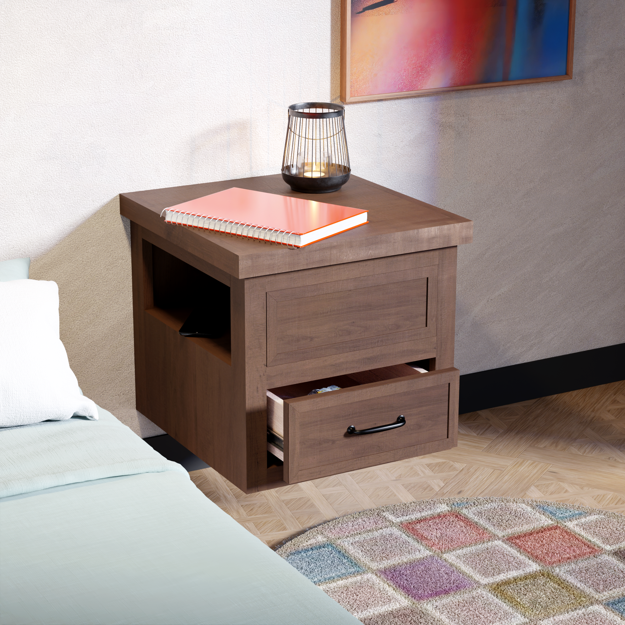 Close-up of a wooden nightstand with a black metal lantern and an orange spiral notebook on top, next to a bed with a light-colored duvet and a pillow, along with a colorful rug and an abstract painting on the wall.